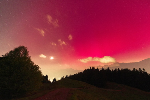 View of the rare red aurora borealis glowing in the starry night sky over the silhouetted forest and hills of the Valtellina valley Sondrio Lombardy Italy. View of the rare red aurora borealis glowing in the starry night sky over the silhouetted forest and hills of the Valtellina valley Sondrio Lombardy Italy.