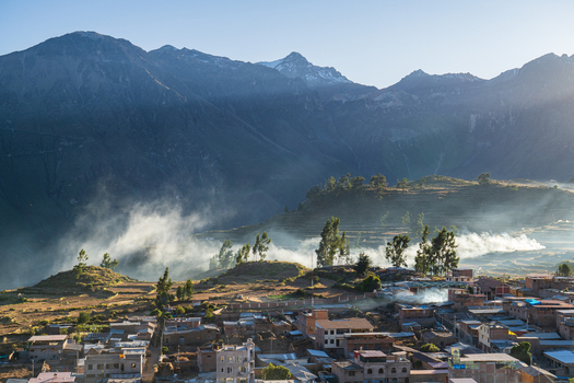 View of the town of Cabanaconde nestled in the Andes mountains with terraced fields rising mist and rugged peaks under a clear sky in Cabanaconde Arequipa Peru.