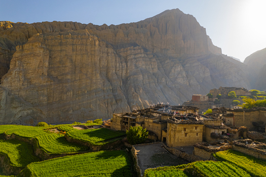 Aerial view of a traditional village nestled in the Himalayas with vibrant green terraced fields stone houses and towering rugged mountain cliffs in Nepal.