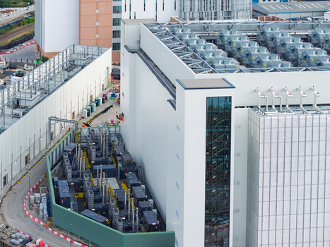Aerial view of a modern data center facility featuring large rooftop cooling units external power generators and industrial infrastructure in the United Kingdom. Aerial view of a modern data center facility featuring large rooftop cooling units external power generators and industrial infrastructure in the United Kingdom.