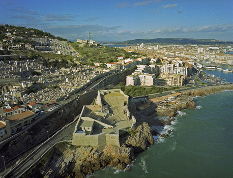 Aerial view of the rugged coastline meets the historic Theatre de la Mer juxtaposed against the sprawling city and verdant hills under a bright sky Marseille France.