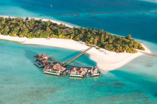 Aerial view of a luxury resort with overwater bungalows connected by wooden walkways to a tropical island with white sandy beaches and lush palm trees near Kudahuvadhoo Dhaalu Atoll Maldives. Aerial view of a luxury resort with overwater bungalows connected by wooden walkways to a tropical island with white sandy beaches and lush palm trees near Kudahuvadhoo Dhaalu Atoll Maldives.