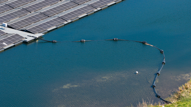 Aerial view of floating solar panels on a calm blue lake with a black floating cable near the grassy shore in Zwolle Overijssel Netherlands. Aerial view of floating solar panels on a calm blue lake with a black floating cable near the grassy shore in Zwolle Overijssel Netherlands.