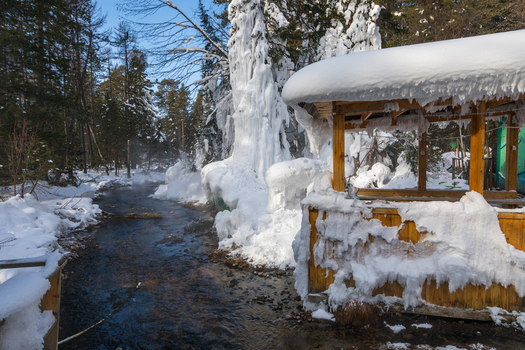 View of Goryachiye Istochniki Khakusy hot spring flowing through a snowy forest with a wooden shelter encased in ice in Severobaykal skiy Rayon Respublika Buryatiya Russia.