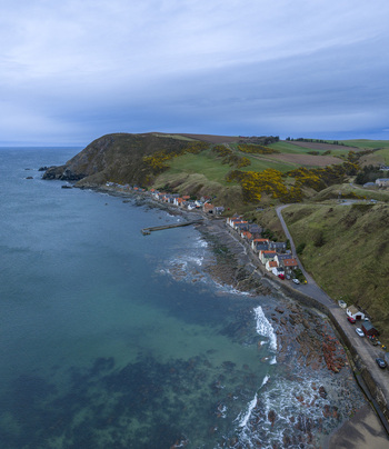 Aerial view of the historic village of Crovie nestled at the base of steep green cliffs along the rugged North Sea coastline Crovie Scotland United Kingdom.