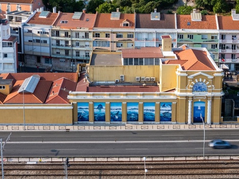 Cruz Quebrada Portugal 25 July 2026 Aerial view of the Vasco da Gama Aquarium with its yellow facade marine life murals and tiled roof near a road and railway tracks.
