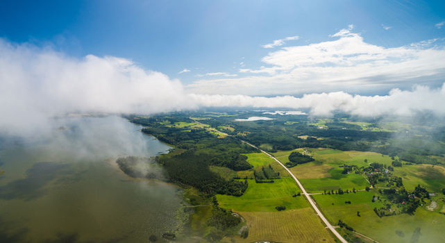 Aerial view of a serene landscape in Latvia featuring a large lake lush green fields dense forests and a winding road under a bright sky with scattered clouds Latvia. Aerial view of a serene landscape in Latvia featuring a large lake lush green fields dense forests and a winding road under a bright sky with scattered clouds Latvia.