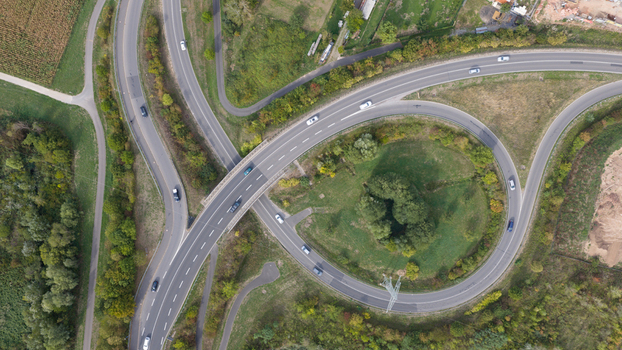 Aerial view of a highway interchange with a circular ramp surrounded by lush green trees and agricultural fields in Grossheubach Bavaria Germany. Aerial view of a highway interchange with a circular ramp surrounded by lush green trees and agricultural fields in Grossheubach Bavaria Germany.