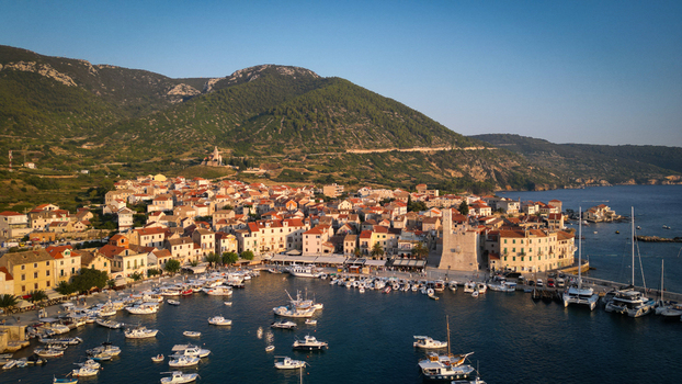 Aerial view of the historic coastal town of Komiza featuring its harbor filled with boats traditional stone houses and lush green hills in Komiza Split Dalmatia County Croatia.