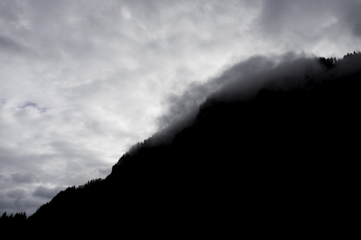 View of the silhouette of a mountain ridge with mist clinging to the slopes under a dramatic overcast sky in Hallstatt Upper Austria Austria. View of the silhouette of a mountain ridge with mist clinging to the slopes under a dramatic overcast sky in Hallstatt Upper Austria Austria.