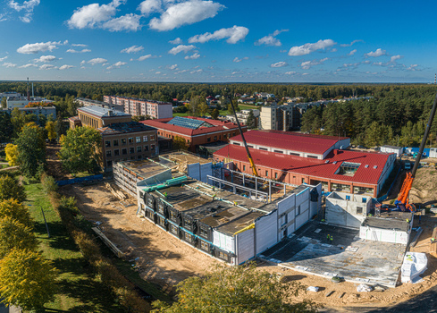 Aerial view of a construction site featuring a new building structure with scaffolding cranes and surrounding green trees and residential buildings in Latvia. Aerial view of a construction site featuring a new building structure with scaffolding cranes and surrounding green trees and residential buildings in Latvia.
