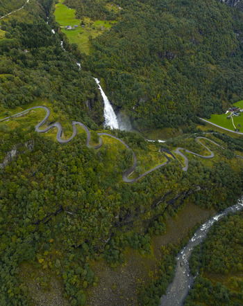 Aerial view of Sivlefossen waterfall and the winding Stalheimskleiva road through lush green forests and a rocky river valley in Voss Vestland Norway.