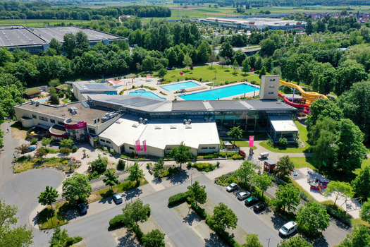 Aerial view of Konigsbad Forchheim featuring outdoor swimming pools colorful water slides and a modern leisure center building surrounded by lush green trees in Forchheim Bayern Germany. Aerial view of Konigsbad Forchheim featuring outdoor swimming pools colorful water slides and a modern leisure center building surrounded by lush green trees in Forchheim Bayern Germany.