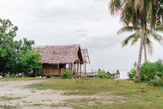 View of a traditional wooden hut with a thatched roof and a wooden pier extending into the sea at Raja Ampat island in Southwest Papua Indonesia. View of a traditional wooden hut with a thatched roof and a wooden pier extending into the sea at Raja Ampat island in Southwest Papua Indonesia.