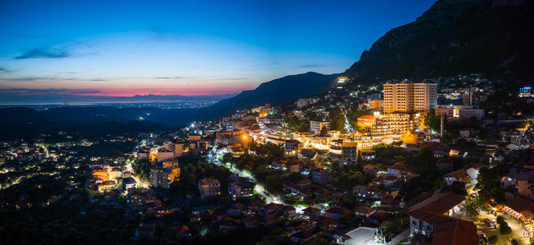 Aerial view of the illuminated city at twilight with glowing street lights and buildings nestled against mountain slopes under evening sky Kruje Durres County Albania.