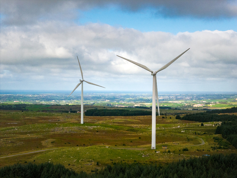 Aerial view of Hog Jaeren vindkraftverk wind turbines standing in the rolling green landscape with a distant coastline under a cloudy sky in Ha Municipality Rogaland Norway.