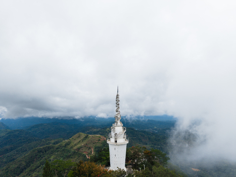 Aerial view of Ambuluwawa Tower rising above misty green hills and lush tropical vegetation under a cloudy sky in Gampola Central Province Sri Lanka. Aerial view of Ambuluwawa Tower rising above misty green hills and lush tropical vegetation under a cloudy sky in Gampola Central Province Sri Lanka.