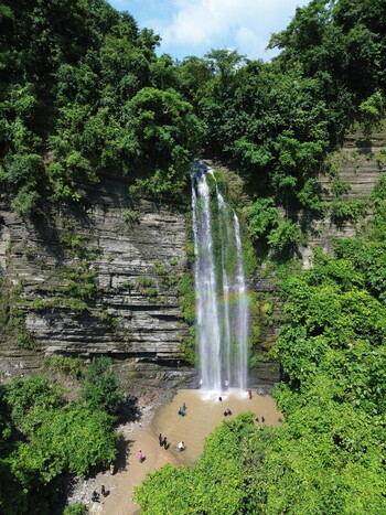 Aerial view of the Sitakund waterfall cascading down rocky cliffs surrounded by dense green forest with people swimming in the pool below in Sitakund Chittagong Division Bangladesh. Aerial view of the Sitakund waterfall cascading down rocky cliffs surrounded by dense green forest with people swimming in the pool below in Sitakund Chittagong Division Bangladesh.