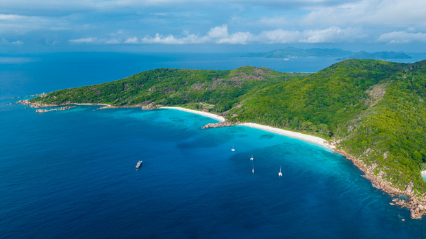 Aerial view of the turquoise waters and white sand beach of Anse Reunion surrounded by lush green hills in Anse Reunion La Digue Seychelles.
