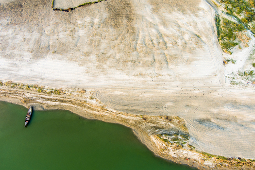 Aerial view of a small wooden boat moored along the sandy riverbank of the Padma River with tire tracks visible on the shore in Rajshahi Rajshahi Division Bangladesh.