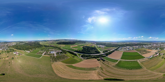 Aerial view of agricultural fields green meadows and the surrounding countryside under a bright sun and blue sky in Lyss Canton of Bern Switzerland.