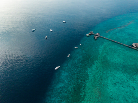 Aerial view of the dramatic contrast between the deep blue ocean and vibrant turquoise shallows around a pier and scattered boats Hoarafushi Thiladhunmathee Uthuruburi Maldives. Aerial view of the dramatic contrast between the deep blue ocean and vibrant turquoise shallows around a pier and scattered boats Hoarafushi Thiladhunmathee Uthuruburi Maldives.