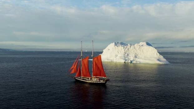 Aerial view of sailboat with red sails near iceberg Greenland. Aerial view of sailboat with red sails near iceberg Greenland.