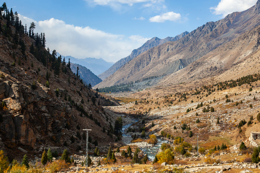 View of Astore Valley with a winding river rocky slopes scattered pine trees and autumn foliage under a blue sky in Astore Gilgit Pakistan. View of Astore Valley with a winding river rocky slopes scattered pine trees and autumn foliage under a blue sky in Astore Gilgit Pakistan.