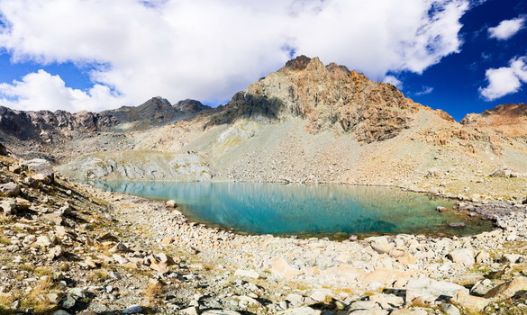 View of a turquoise alpine lake surrounded by rugged rocky mountains under a blue sky with white clouds in Chiesa in Valmalenco Lombardy Italy. View of a turquoise alpine lake surrounded by rugged rocky mountains under a blue sky with white clouds in Chiesa in Valmalenco Lombardy Italy.