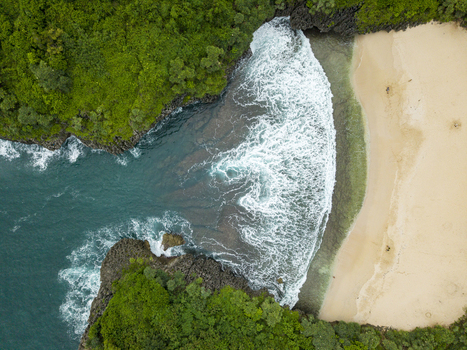 Aerial view of the Sedahan Beach where turquoise waters meet the shore with foamy waves framed by lush green cliffs Gunungkidul Regency Indonesia. Aerial view of the Sedahan Beach where turquoise waters meet the shore with foamy waves framed by lush green cliffs Gunungkidul Regency Indonesia.