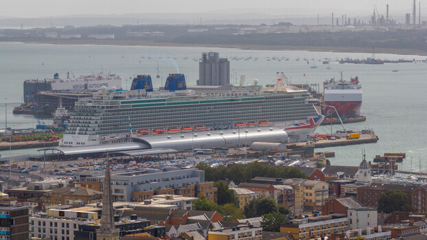 Aerial view of a large cruise ship docked at the port of Southampton with industrial buildings and urban rooftops in the background in Southampton England United Kingdom. Aerial view of a large cruise ship docked at the port of Southampton with industrial buildings and urban rooftops in the background in Southampton England United Kingdom.