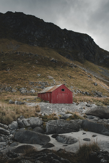View of a red wooden shed situated on the rocky shore of Vikten Beach at the foot of a steep mountain in Vikten Nordland Norway.