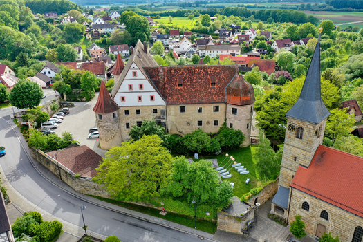 Aerial view of Schloss Wiesenthau castle with its historic stone towers and red roofs next to a church spire in a green village Wiesenthau Bayern Germany. Aerial view of Schloss Wiesenthau castle with its historic stone towers and red roofs next to a church spire in a green village Wiesenthau Bayern Germany.