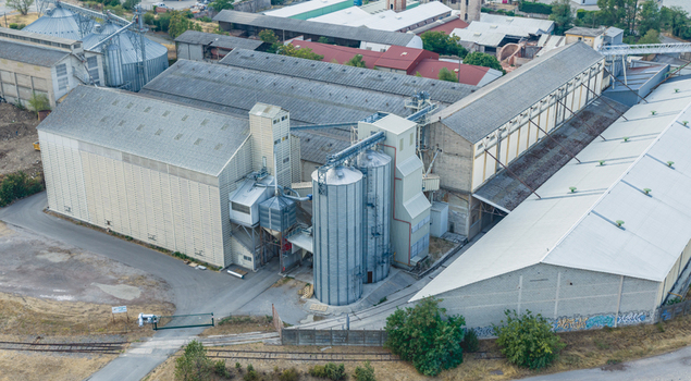 Aerial view of an industrial grain storage and processing facility with metal silos warehouses and conveyor systems in Le Pouzin Auvergne Rhone Alpes France.