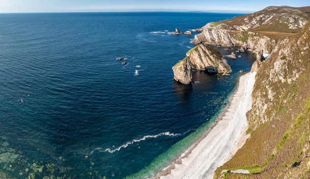 Aerial view of the rugged coastline and sea stacks at Glenlough Bay with steep cliffs and a pristine beach in Ardara County Donegal Ireland.