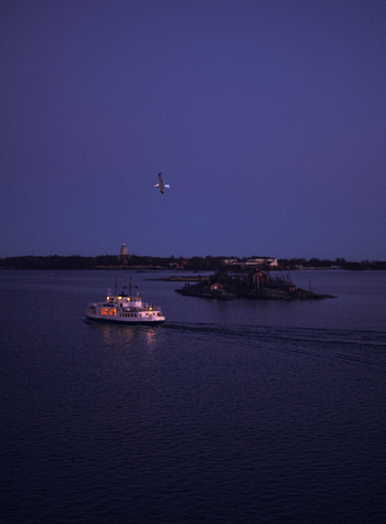 View of a lighted ferry boat cruising through the harbor at dusk with a small island and the city skyline in the background Helsinki Uusimaa Finland. View of a lighted ferry boat cruising through the harbor at dusk with a small island and the city skyline in the background Helsinki Uusimaa Finland.