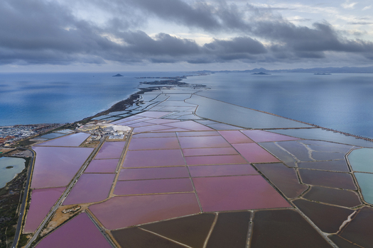 Aerial view of the vibrant pink and brown salt ponds juxtaposed against the blue sea under a cloudy sky San Pedro del Pinatar Region of Murcia Spain. Aerial view of the vibrant pink and brown salt ponds juxtaposed against the blue sea under a cloudy sky San Pedro del Pinatar Region of Murcia Spain.