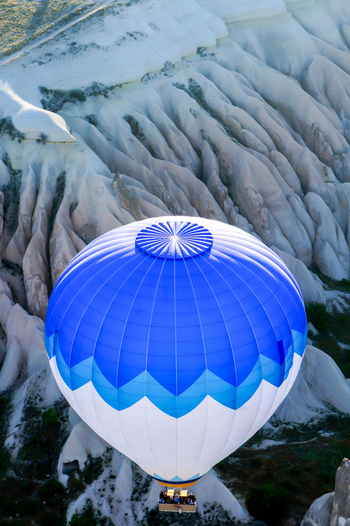 Aerial view of a blue and white hot air balloon with people in the basket over the unique volcanic rock formations and fairy chimneys of Cappadocia in Kayseri Kayseri Turkiye. Aerial view of a blue and white hot air balloon with people in the basket over the unique volcanic rock formations and fairy chimneys of Cappadocia in Kayseri Kayseri Turkiye.