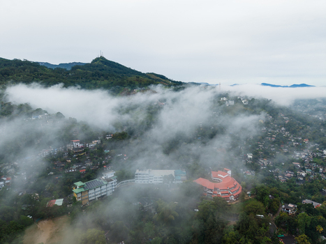 Aerial view of Kandy city nestled among lush green hills partially obscured by thick white clouds and mist under an overcast sky Kandy Central Province Sri Lanka. Aerial view of Kandy city nestled among lush green hills partially obscured by thick white clouds and mist under an overcast sky Kandy Central Province Sri Lanka.