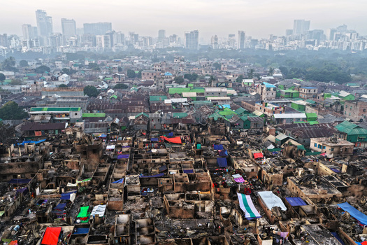 Aerial view of Korail Basti showing dense housing with colorful tarps and fire damaged structures against the modern skyline of Dhaka Dhaka Division Bangladesh.