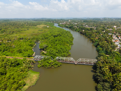 Aerial view of a metal truss bridge spanning a wide river surrounded by lush tropical vegetation and palm trees in Galle Southern Province Sri Lanka.