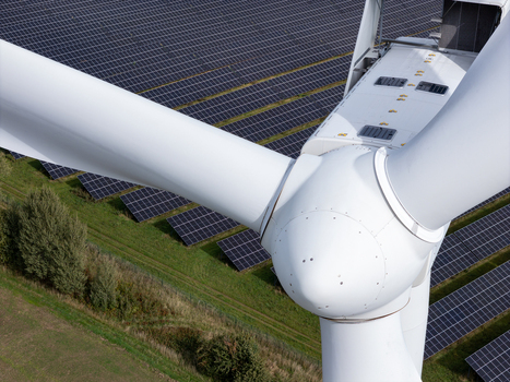 Aerial view of a wind turbine hub and blades with a large solar panel farm in the background in Poland.