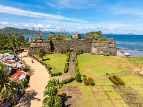 Aerial view of Fort Santa Isabel a historic stone fortress with people on the path green lawns and palm trees overlooking the blue sea in Taytay Mimaropa Philippines.