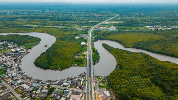 Aerial view of the Kwa Ibo River winding through lush mangrove forests and coastal vegetation with a bridge crossing the water and a nearby settlement in Kwa Ibo Akwa Ibom Nigeria.