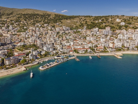 Aerial view of Saranda coastal city featuring a busy harbor with docked boats dense urban architecture and rolling hills under a clear blue sky in Saranda Vlore County Albania. Aerial view of Saranda coastal city featuring a busy harbor with docked boats dense urban architecture and rolling hills under a clear blue sky in Saranda Vlore County Albania.