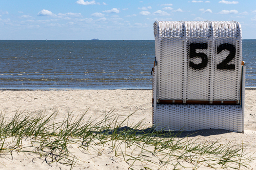 View of a white wicker beach chair with number 52 on the sandy Strand Schillig beach overlooking the North Sea under a blue sky in Wangerland Niedersachsen Germany. View of a white wicker beach chair with number 52 on the sandy Strand Schillig beach overlooking the North Sea under a blue sky in Wangerland Niedersachsen Germany.