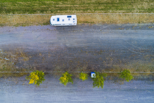 Aerial view of a white camper van parked on a gravel lot beside a green field and a line of trees in Vanersnas Vastra Gotalands lan Sweden. Aerial view of a white camper van parked on a gravel lot beside a green field and a line of trees in Vanersnas Vastra Gotalands lan Sweden.