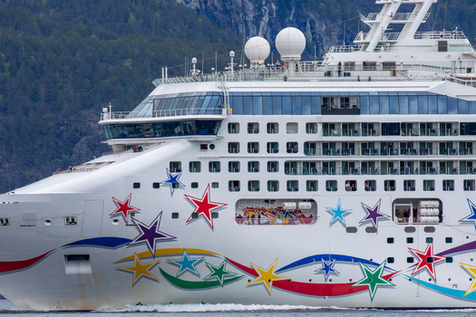 View of a cruise ship with colorful star livery sailing through a fjord with forested mountains in the background in Stranda More og Romsdal Norway.