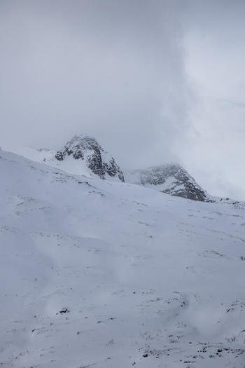 View of snow covered mountain peaks under a thick layer of grey clouds in the arctic wilderness Ersfjord Troms Norway. View of snow covered mountain peaks under a thick layer of grey clouds in the arctic wilderness Ersfjord Troms Norway.