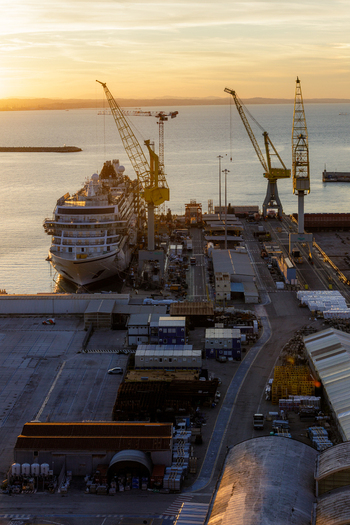 Aerial view of Ancona Port with a large cruise ship docked alongside industrial cranes storage containers and warehouses under the warm light of sunset in Ancona Marche Italy. Aerial view of Ancona Port with a large cruise ship docked alongside industrial cranes storage containers and warehouses under the warm light of sunset in Ancona Marche Italy.